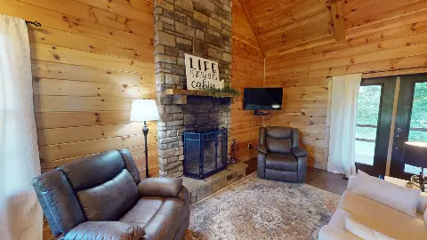 Living room with stone fireplace, recliners and a Life Is Better at the Cabin sign