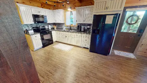 Kitchen with white cabinets, black appliances and front door